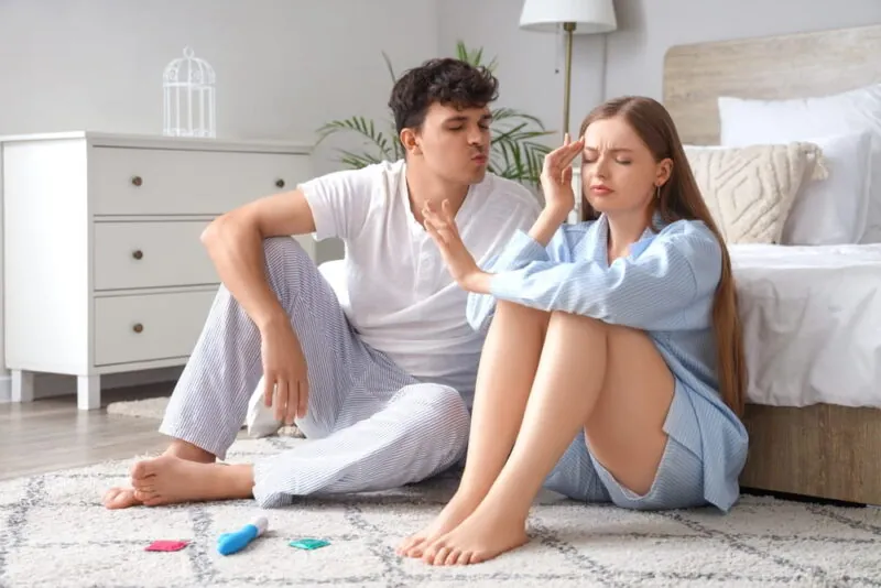 Displeased young woman with husband trying to kiss her in bedroom. Sexual problems concept