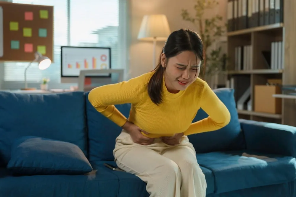 Young businesswoman is experiencing severe menstrual cramps while sitting on a sofa in her home office