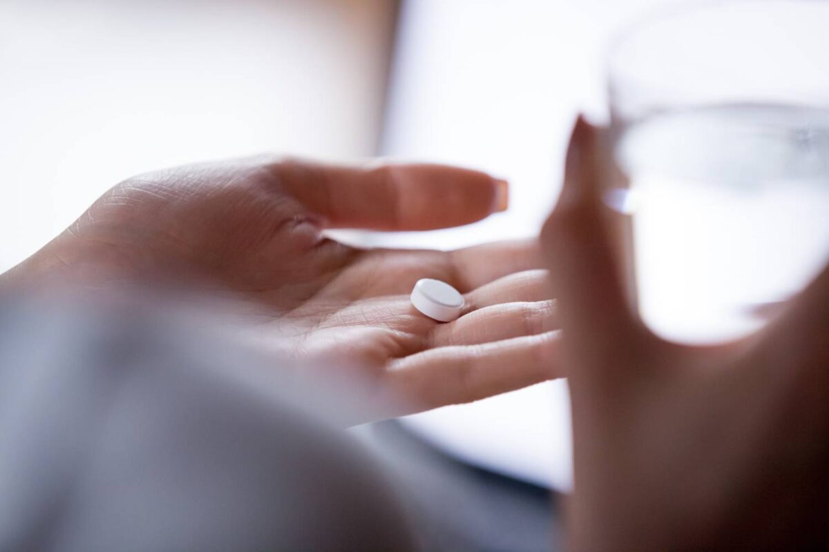 woman holding pill in hand with water
